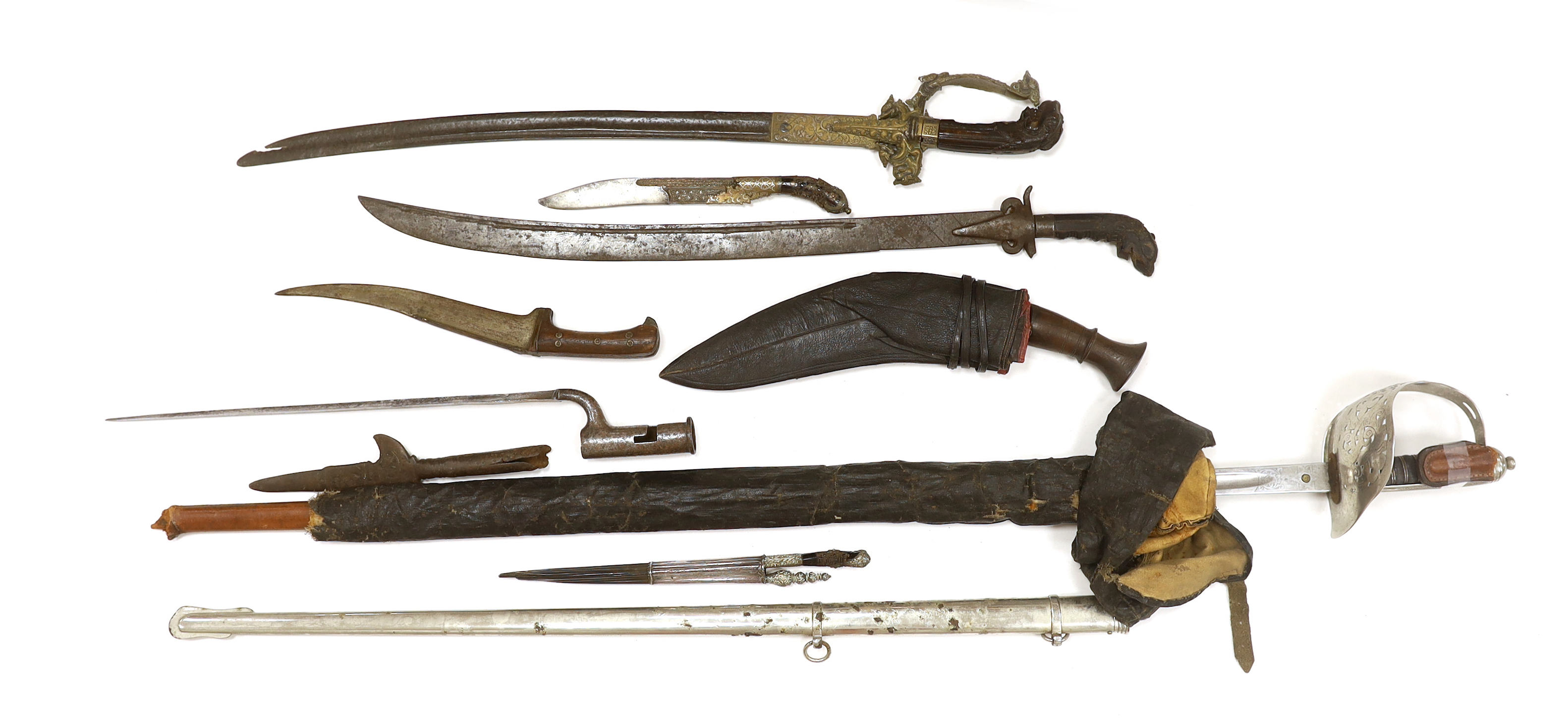 Two Sinhalese daggers and a kukri, a silver inlaid Kirichchiya dagger, together with another in a scabbard with a long pin, another dagger with a wooden handle, a head of a brass inlaid iron pole arm, a George V 1897 pat